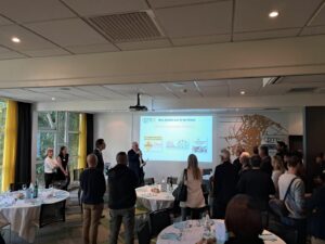 Conférence CPME 91, homme devant l'assemblée debout avec écran de présentation derrière. Auditeurs debout devant lui autour de tables de déjeuner. Photo prise par le GEYVO recrutement flexible en temps partagé.