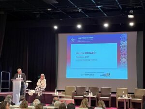 Scène des 30 de CAP Emploi 78 - IHY au Campus Oxygène Factory – Les Mureaux. 1 homme debout au pupitre, 1 femme assise, 1 présentation projetée en arrière plan sur l'écran